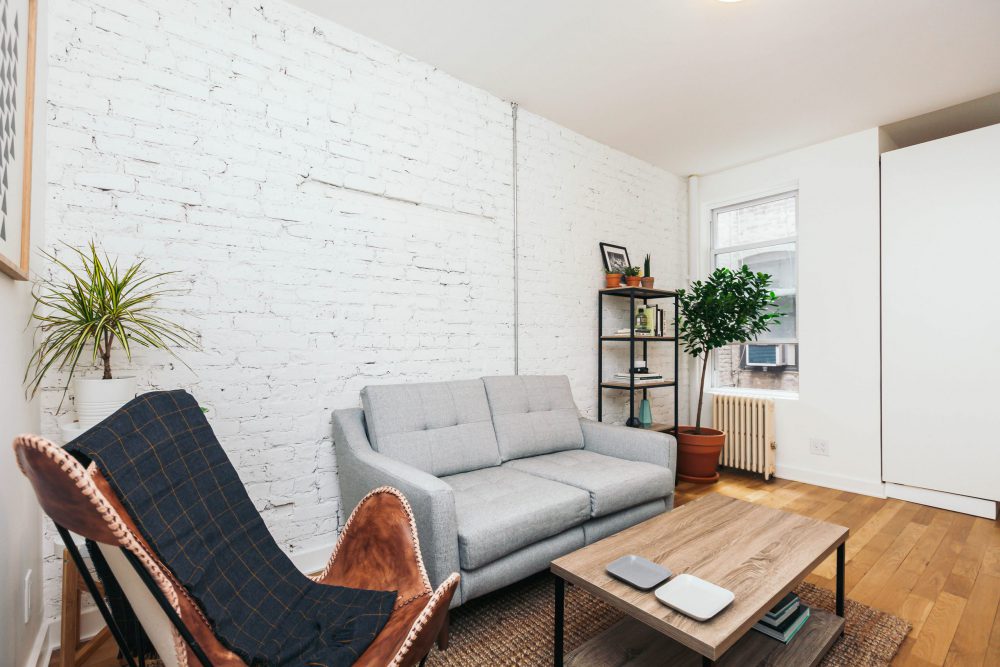 living room with sofa, butterfly chair, wood coffee table, white painted brick wall