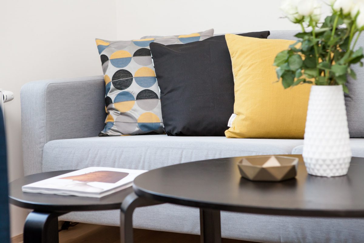 A small space living room with color coordinated throw cushions and a small coffee table with plant and ashtray.