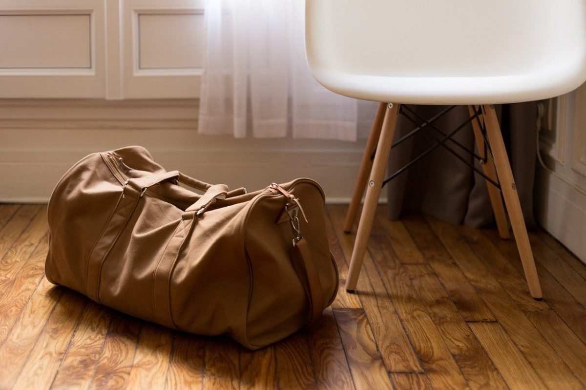 a tan duffel bag on the ground beside a white chair