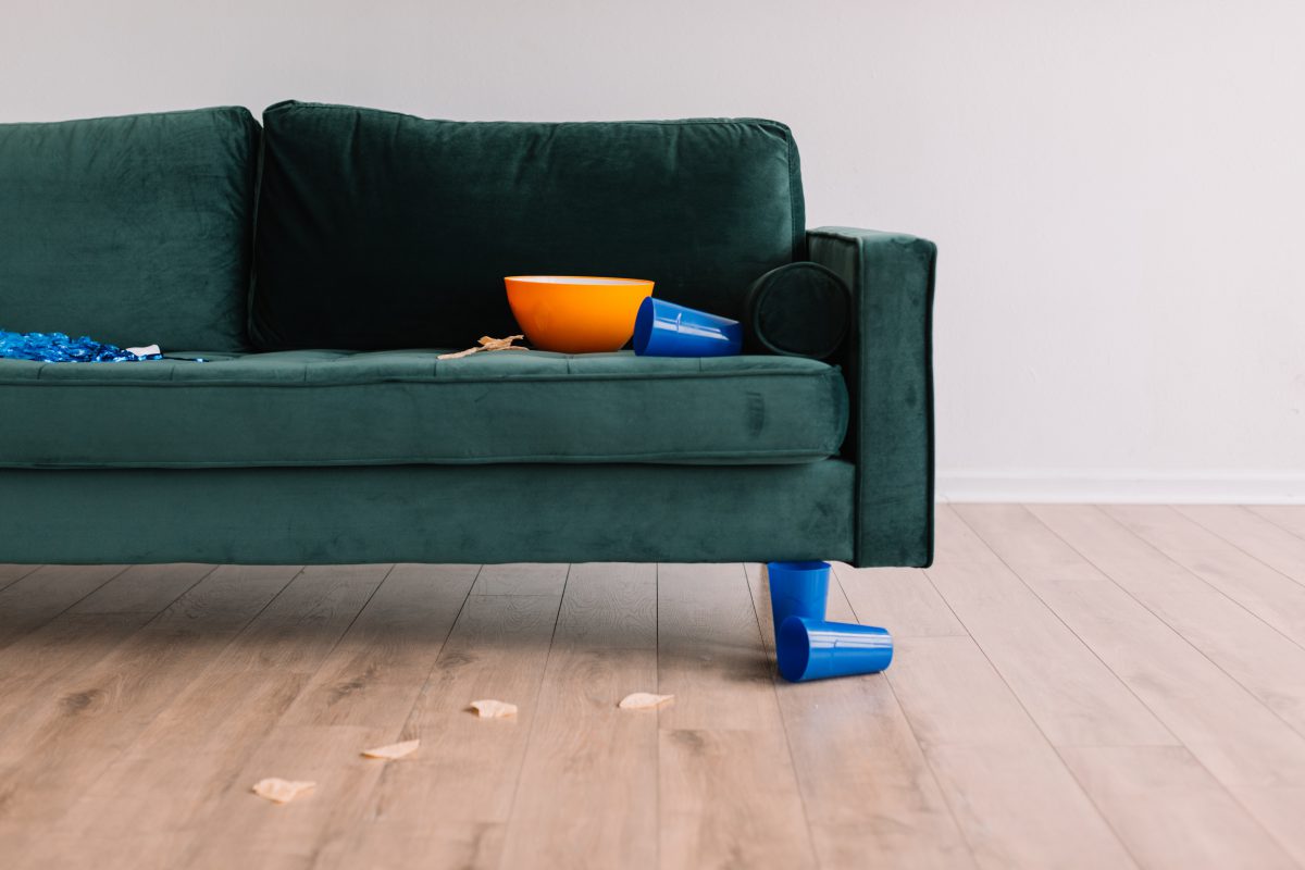 a dark teal couch with spilled chips on the ground and an overturned plastic cup