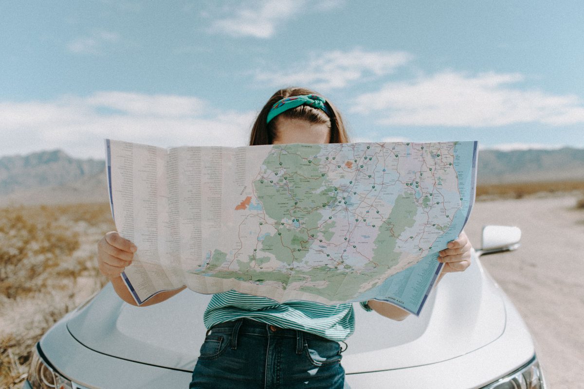 A woman looks down at a map and leans against the hood of a car.